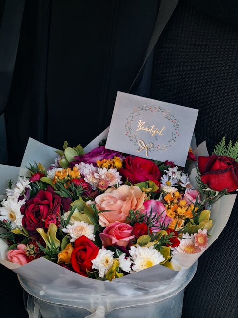 A vibrant floral bouquet arranged with a variety of fresh flowers, including red and deep pink roses, peach carnations, white daisies, and small yellow blossoms, all nestled among lush green foliage.